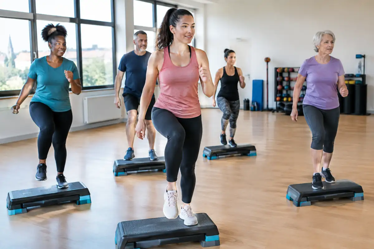 Cours de step fitness en salle : une participante monte sur sa plateforme pendant que le groupe suit la chorégraphie.