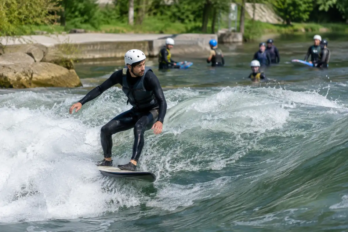 Surfeur en rivière sur une vague stationnaire, équipé d’une planche compacte, d’un casque, d’un gilet et d’une combinaison néoprène.