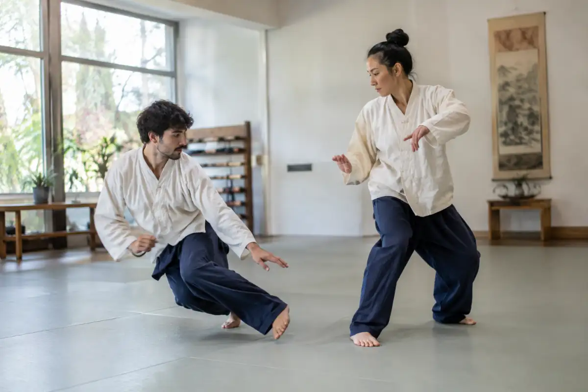 Deux pratiquants de Taekkyeon travaillent un balayage et un déplacement rythmé dans une salle d’arts martiaux.