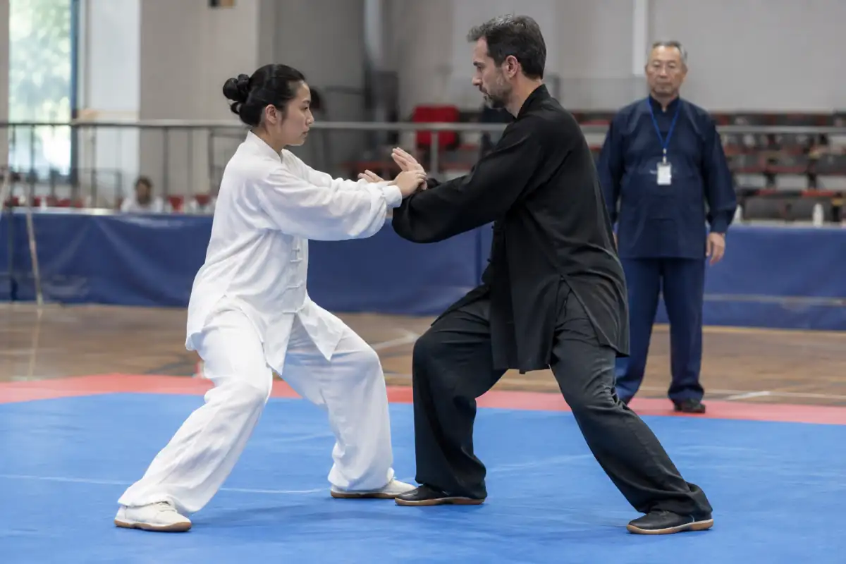 Deux compétiteurs de tai-chi-chuan travaillent le tuishou sur une aire délimitée, sous le regard attentif d’un arbitre.
