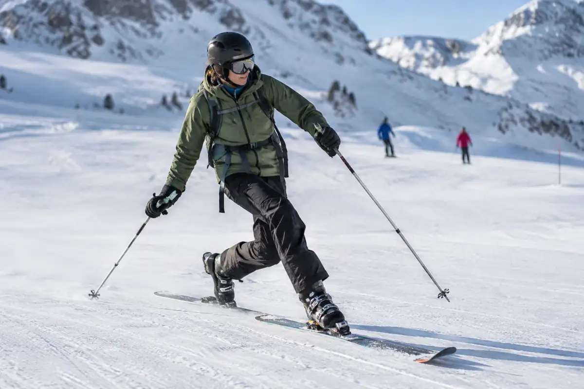Skieur en télémark enchaînant un virage en fente sur une piste damée, talon arrière levé et genoux fléchis.