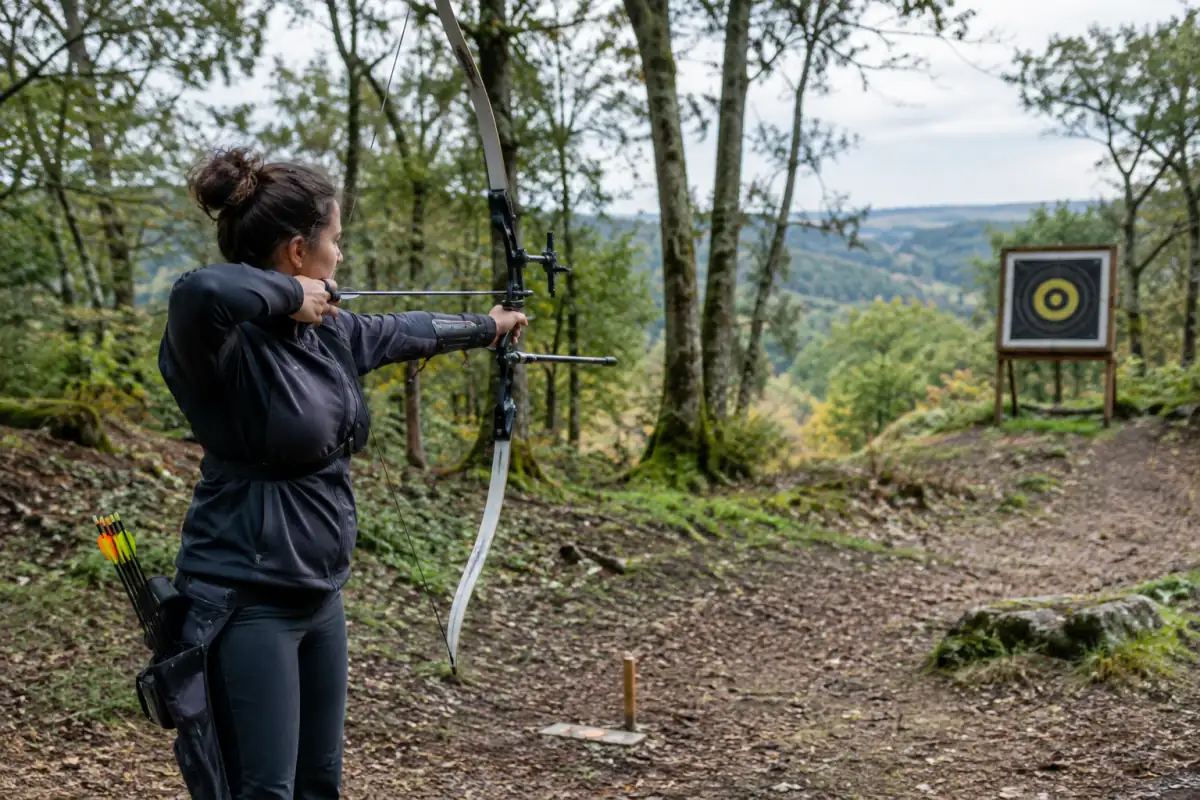 Un archer vise un blason noir et jaune sur un parcours boisé lors d’une séance de tir à l’arc en campagne.