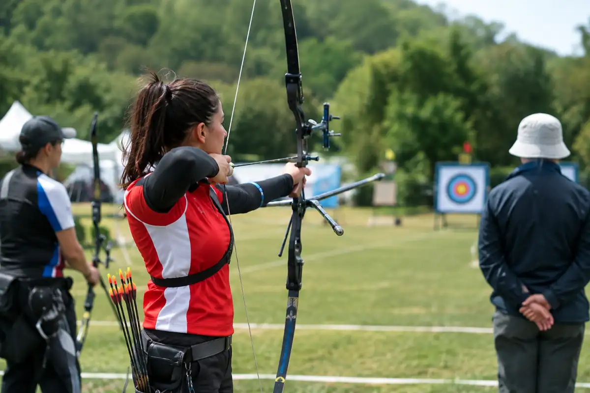 Archer en compétition extérieure tirant vers un blason depuis la ligne, avec les autres participants en attente derrière lui.