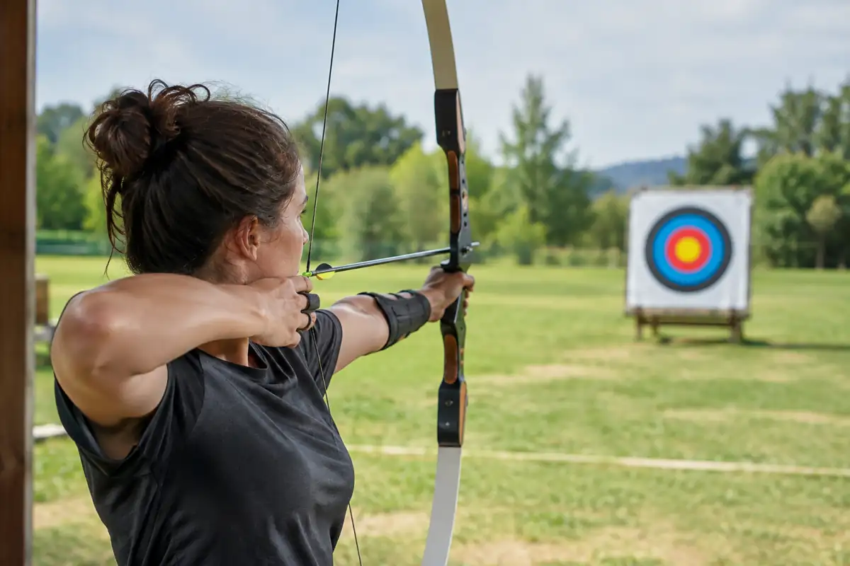 Archer en arc classique à pleine allonge, main de corde ancrée sous la mâchoire et viseur aligné sur une cible.