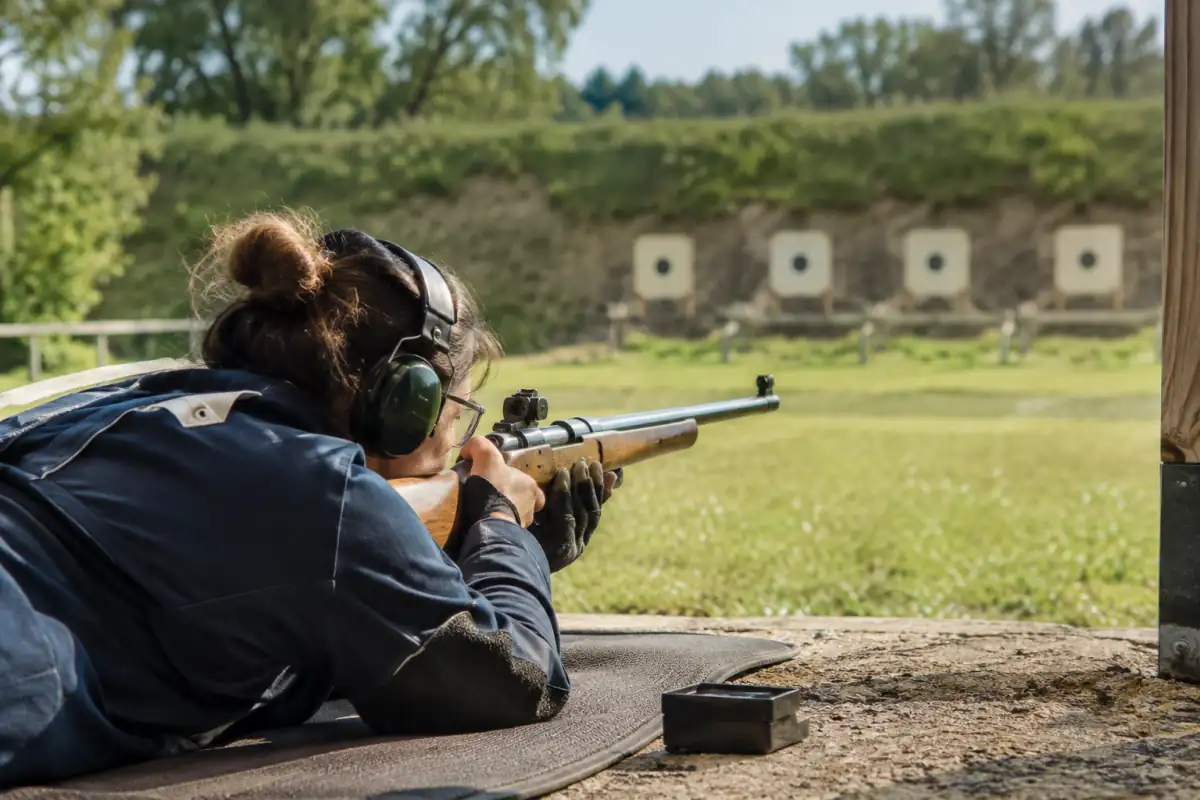 Un tireur pratique le tir aux armes réglementaires au fusil, couché sur un pas de tir extérieur avec ses protections.