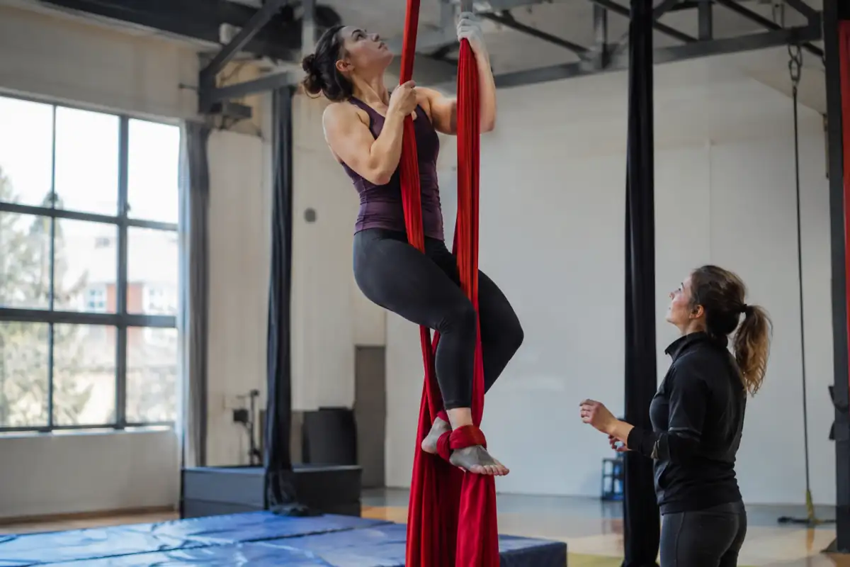 Une pratiquante grimpe sur un tissu aérien dans une école de cirque équipée de matelas de réception.
