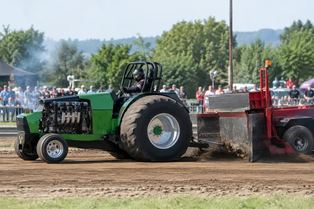 Tractor pulling : un tracteur préparé tire une remorque à poids mobile sur une piste en terre.