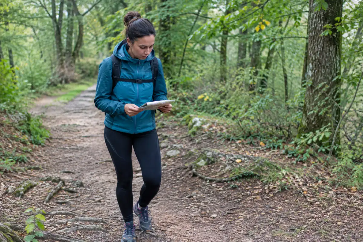 Débutant en trail marchant sur un chemin forestier peu pentu, carte en main, lors d’une première sortie nature.