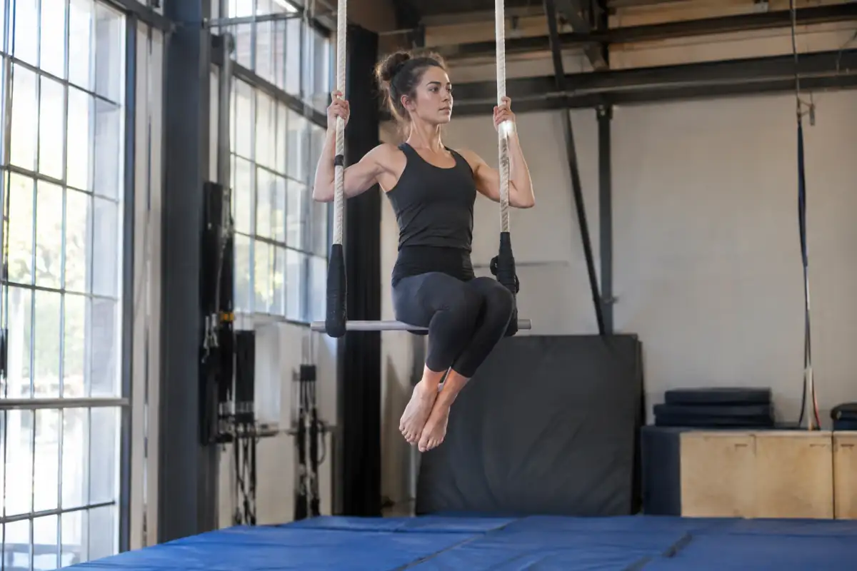 Une élève de trapèze aérien travaille une suspension par les genoux au-dessus de tapis dans une école de cirque.