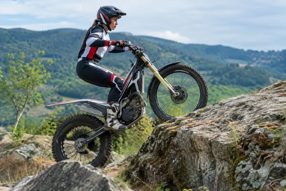 Pilote en équilibre debout sur sa moto de trial, franchissant un rocher sur un terrain aménagé en France.