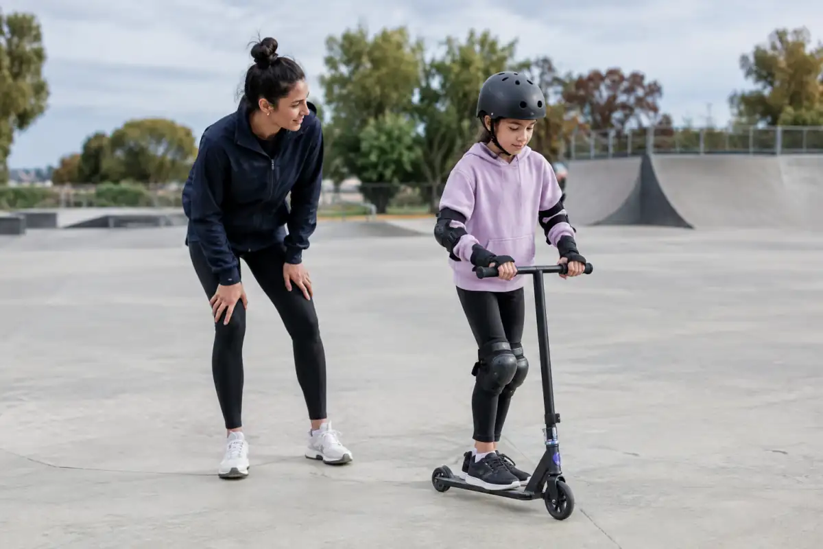 Débutant équipé d’un casque et de protections travaillant son équilibre en trottinette freestyle sur une zone plane dégagée.