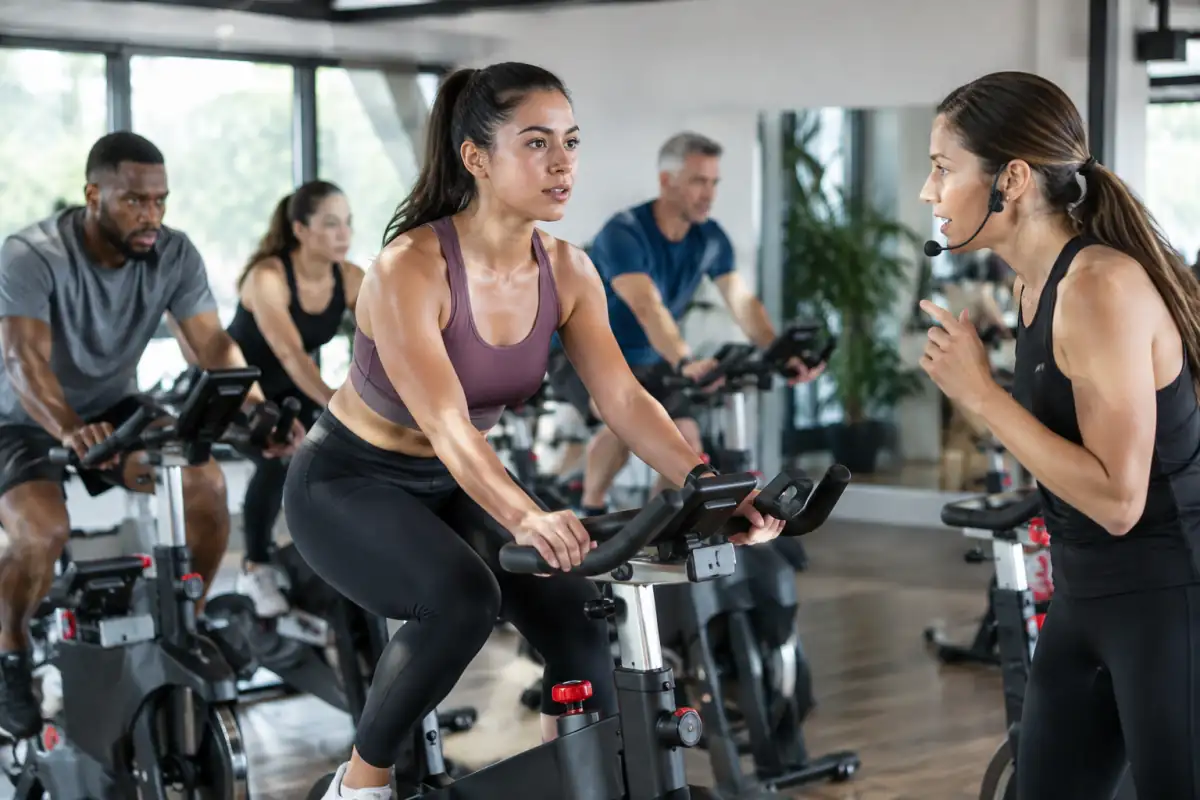 Participant pédalant assis sur un vélo de studio pendant qu’un enseignant donne les consignes de cadence et de résistance.
