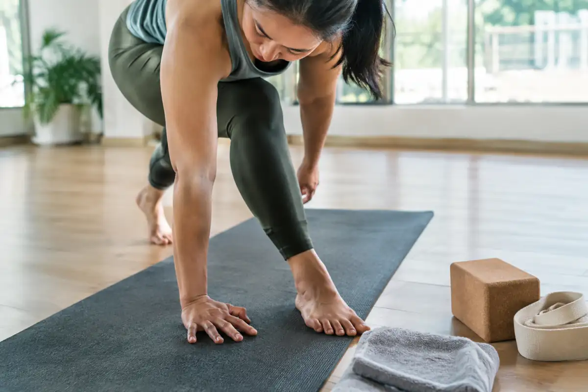 Une pratiquante teste l’adhérence d’un tapis de vinyasa, avec une brique, une sangle et une serviette posées à côté.