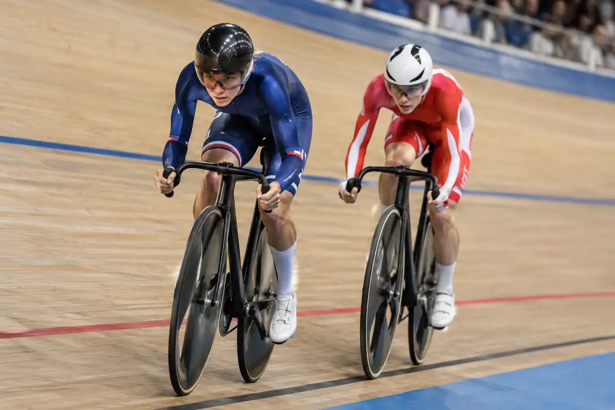 Deux cyclistes en duel de vitesse sur piste accélèrent sur leurs vélos à pignon fixe dans un vélodrome couvert.