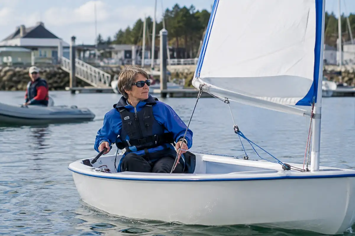 Un navigateur en situation de handicap barre un dériveur Hansa 303 adapté lors d’une séance de voile adaptée près d’un ponton.
