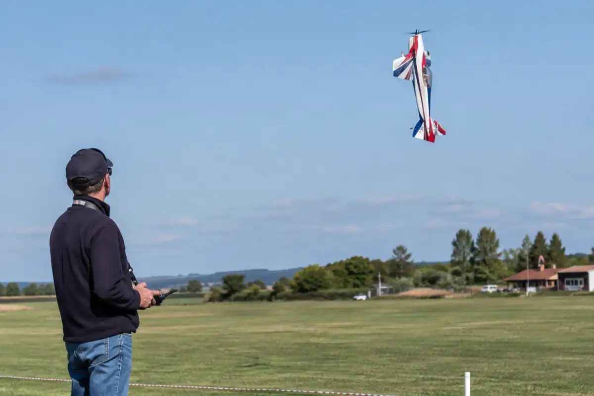 Un pilote réalise une figure de voltige aéromodéliste avec un avion radiocommandé au-dessus d’un terrain de club.