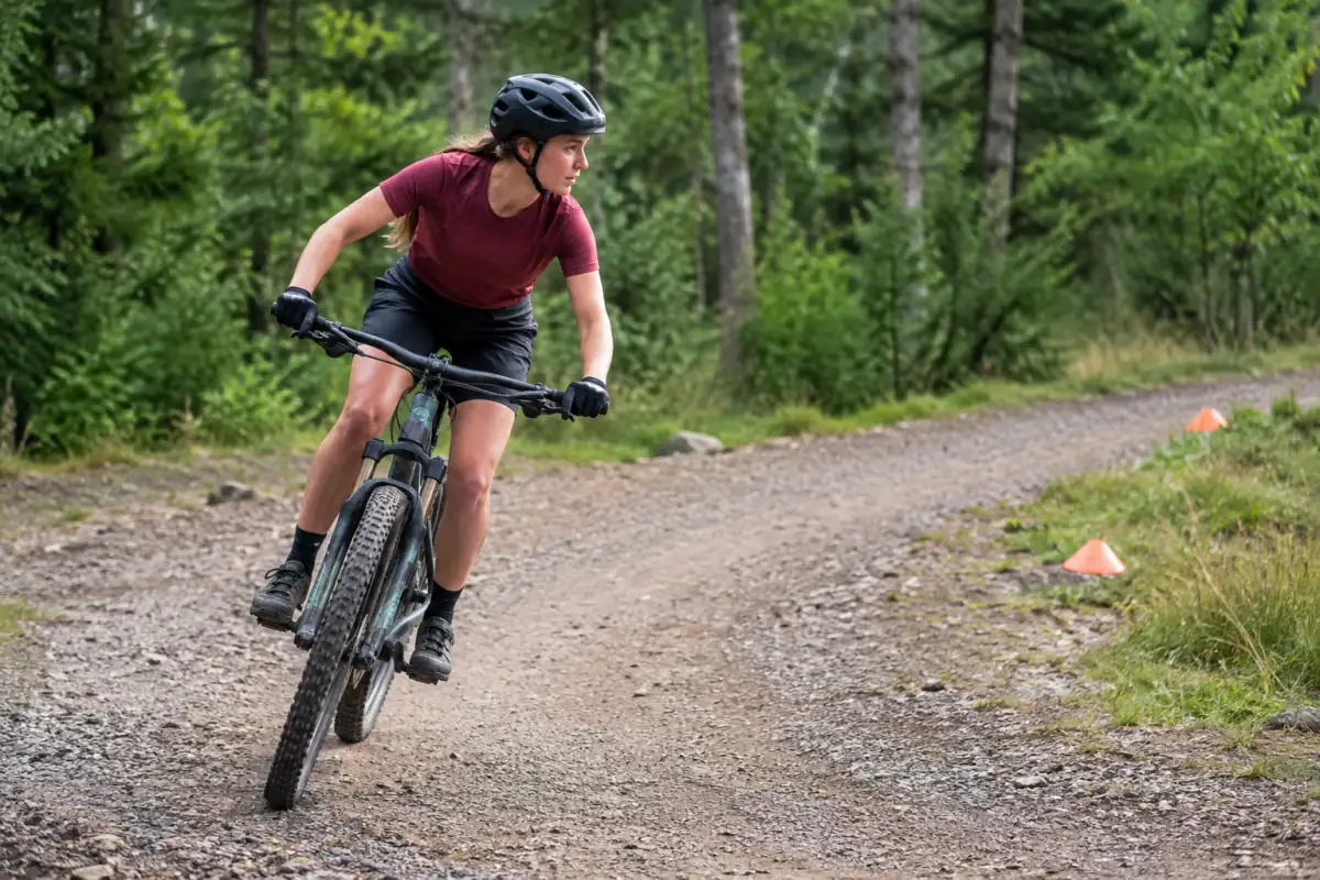 Débutant en VTT cross-country travaillant une position souple et un virage large sur un chemin dégagé.