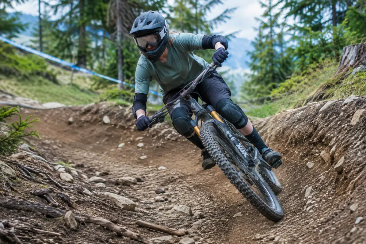 Pilote en casque intégral négociant un virage relevé sur une piste de VTT de descente en montagne.