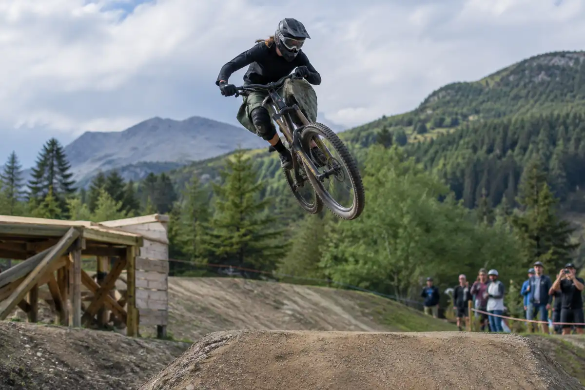 Un pilote de VTT slopestyle, équipé d’un casque intégral et de protections, réalise une figure au-dessus d’un saut en terre.