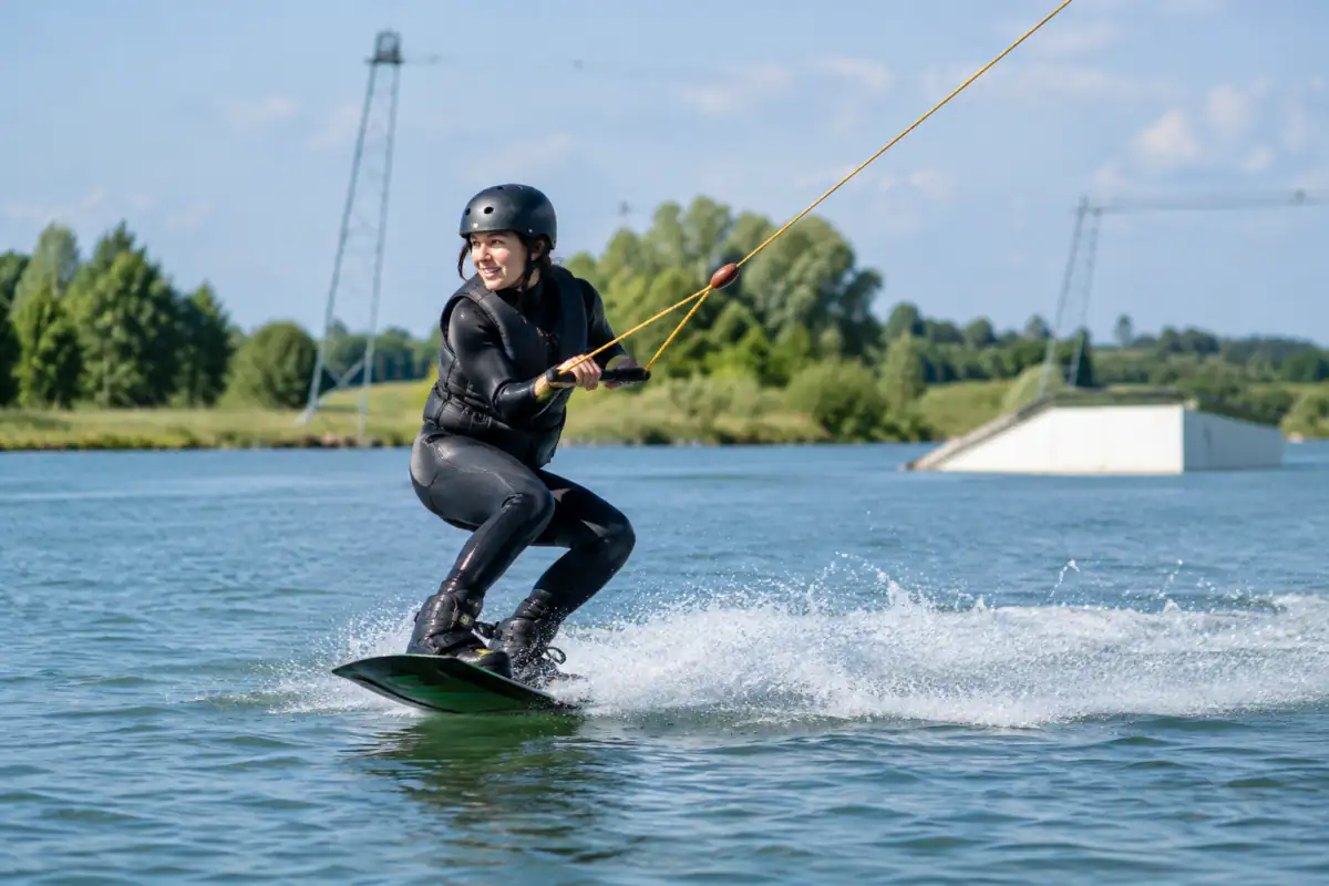 Un pratiquant de wakeboard câble, casque et gilet portés, glisse sur l’eau tracté par un téléski nautique.