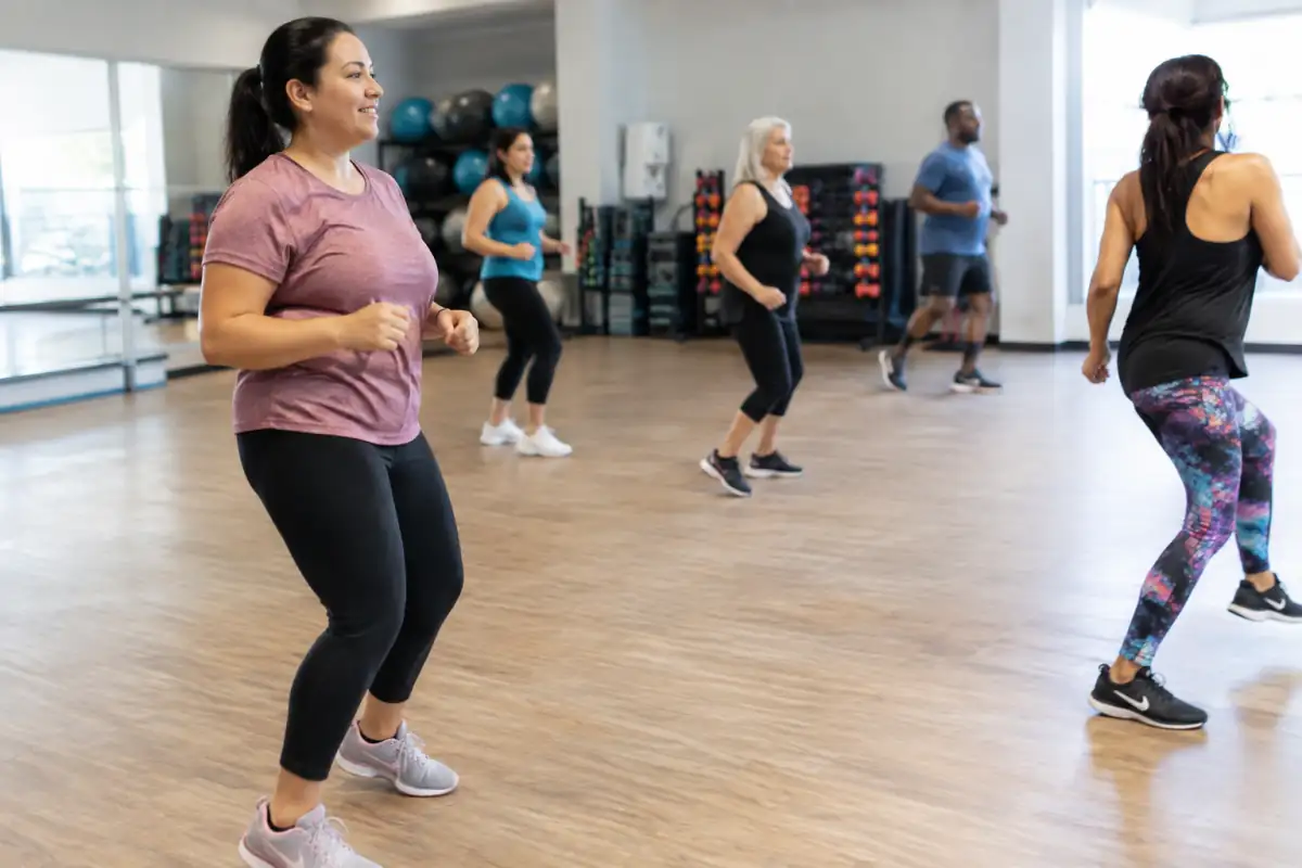 Une débutante suit un pas latéral sans saut dans un cours collectif de Zumba, en gardant l’instructeur bien en vue.