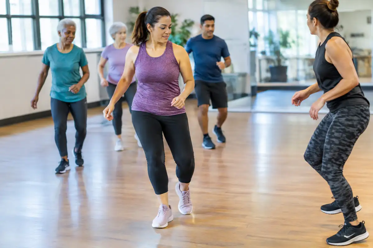 En cours de Zumba, une participante travaille un pas latéral simple et le transfert du poids, bras relâchés et amplitude modérée.